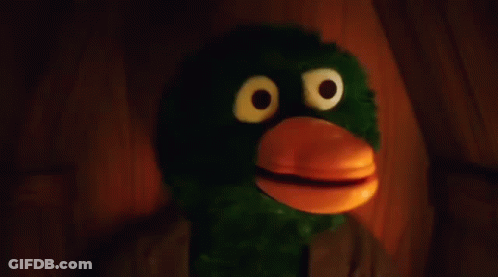 Green And Orange Stuffed Animal With Big Eyes And Beak In Dark Room GIF