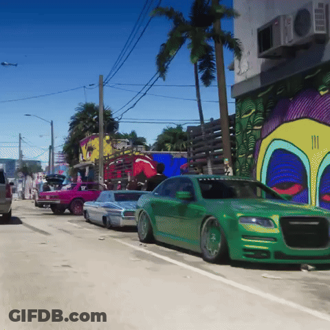 Green Car Parked In Front Of Building With Graffiti GIF