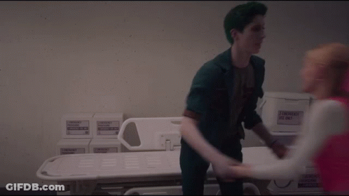 Green-Haired Man Holding Woman's Hand By Hospital Bed GIF