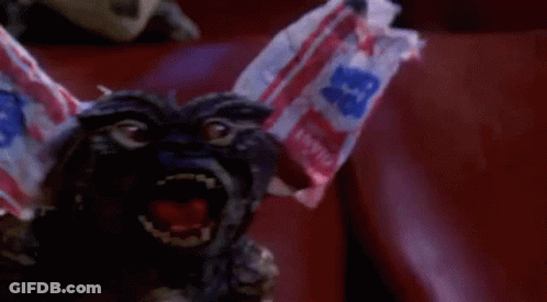 Gremlin Sitting In Red Chair With Candy Bag On Head GIF