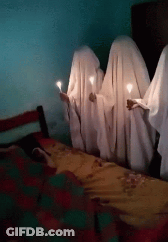 Group Covered In White Sheets Holding Candles In Front Of Bed GIF