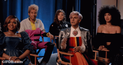 Group In Director's Chairs With Man In Rainbow Dress GIF