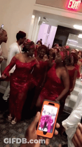 Group In Red Dresses In Front Of Exit Sign GIF