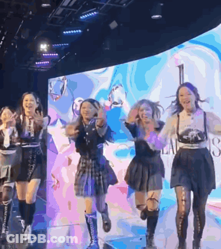 Group Of Girls Dancing On Stage With Screen Saying A GIF