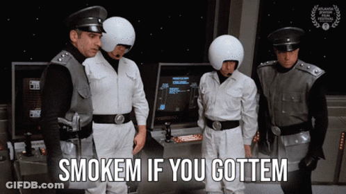 Group Of Men Standing In Front Of Arcade Machine Saying Smokem If You Gottem GIF