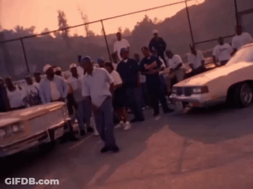 Group Of Men Standing In Parking Lot Surrounded By Cars GIF