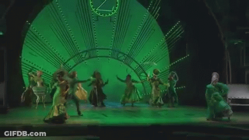 Group Of People Dancing On Stage In Front Of Clock GIF