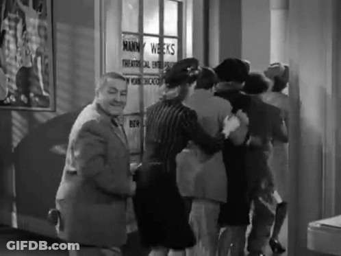 Group Of People In Front Of Mann Weeks Sign GIF