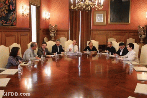 Group Of People Sitting Around Large Wooden Table In Conference Room GIF