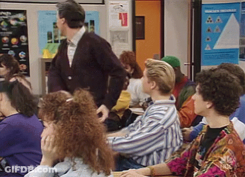 Group Of People Sitting At Desks In Classroom With Man Standing GIF
