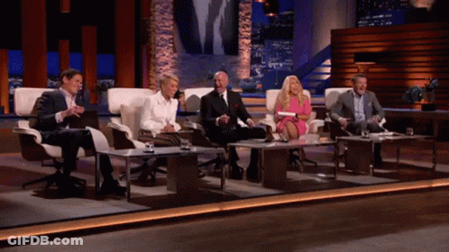 Group Of People Sitting At Tables On Stage GIF