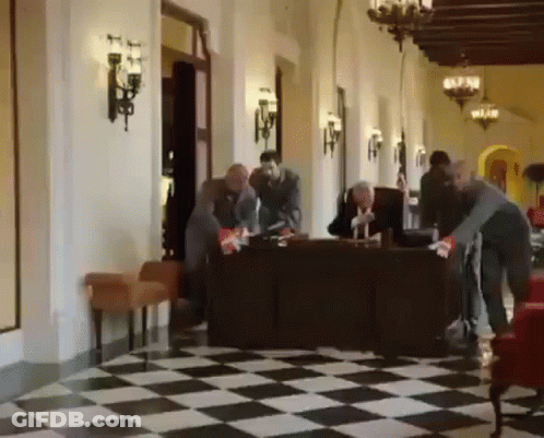 Group Of People Standing Around Table In Hallway With Checkered Floor GIF