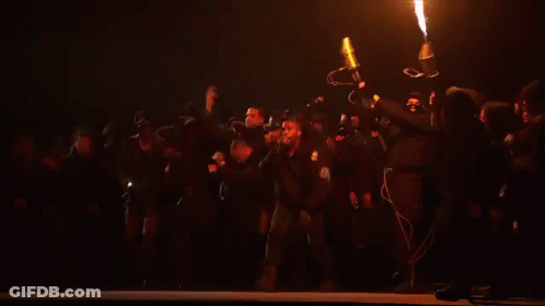 Group Of People Standing On Stage With Large Fire GIF