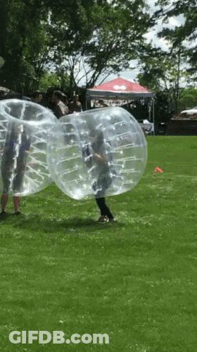 Group Playing Bubble Soccer In Grass GIF