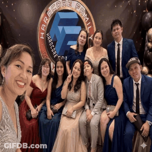 Group Posing In Front Of Hardcore Family Banner GIF