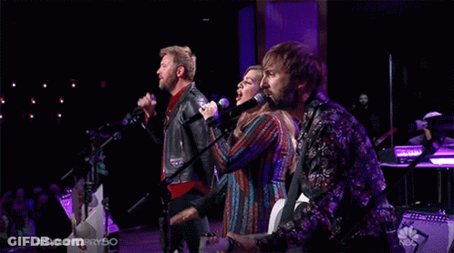 Group Singing Into Microphones On Stage With NBC Logo GIF