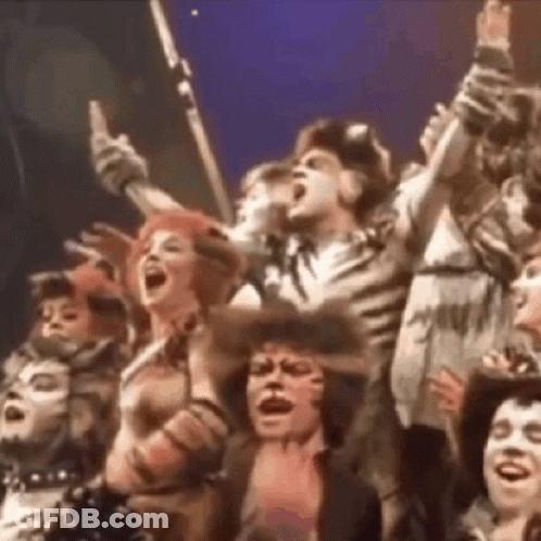 Group Singing On Stage With Arms Raised GIF