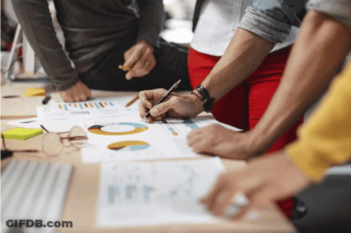 Group Sitting Around Table Looking At Graphs GIF