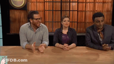 Group Sitting At Table With Hands Folded In Front Of Sign A GIF