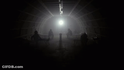 Group Sitting In Dark Room With Light Through Ceiling GIF