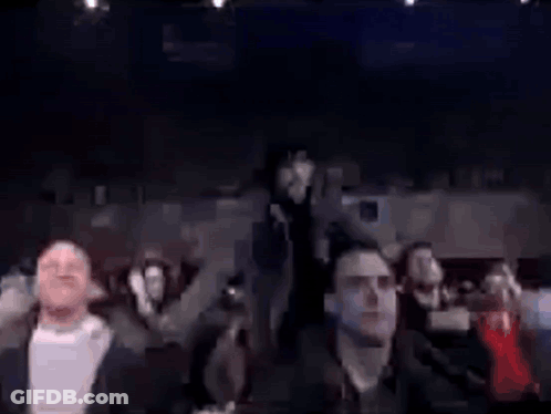Group Sitting In Dark Room With Man Standing In Middle GIF