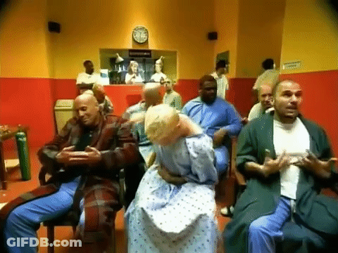 Group Sitting In Waiting Room With Clock At 12:15 GIF