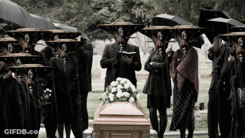 Group Standing Around Coffin In Cemetery With Umbrellas GIF