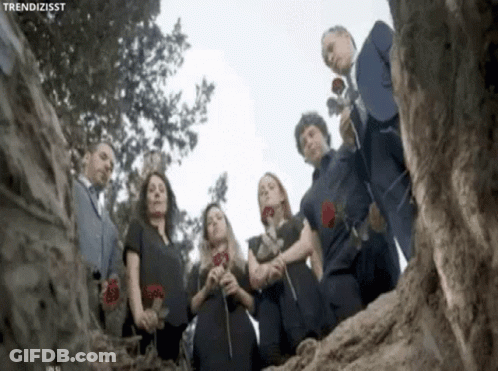 Group Standing In Circle Holding Roses In Front Of Tree GIF