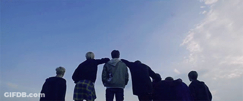 Group Standing In Circle With Arms Around Each Other Against Blue Sky GIF