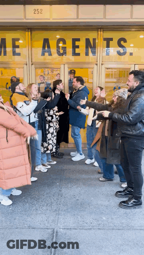 Group Standing In Front Of Agents Building GIF