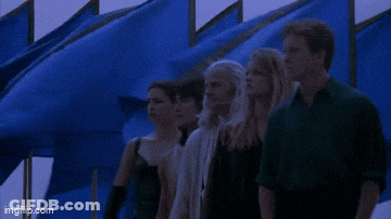 Group Standing In Front Of Blue Flags GIF