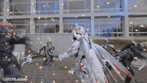 Group Standing In Front Of Building, One In White Cape GIF