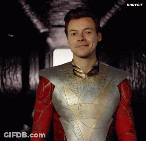 Harry Styles Is Wearing A Superhero Costume And Smiling In A Dark Hallway . GIF