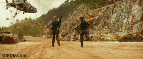 Helicopter Flying Over Dirt Road With Two People Running GIF