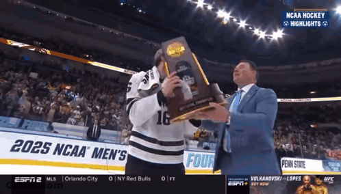 Hockey Player Holding Trophy In Front Of 2025 NCAA Men's Banner GIF