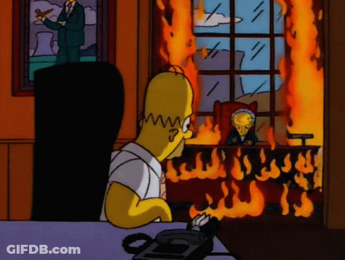 Homer Simpson Is Sitting At A Desk In Front Of A Burning Window GIF
