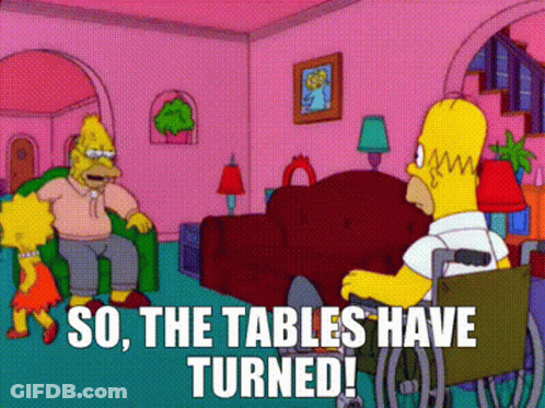 Homer Simpson Is Sitting In A Wheelchair In A Living Room Talking To A Woman . GIF