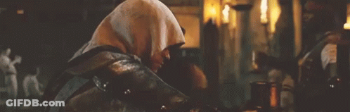 Hooded Man Sitting In Dark Room With Candles GIF