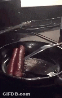 Hot Dogs Are Being Cooked In A Frying Pan With A Spatula GIF