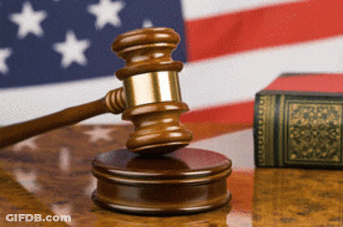 Judge's Gavel On Wooden Table In Front Of American Flag GIF