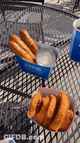Ketchup 'S Pretzels And Onion Rings Are On A Table Outside GIF
