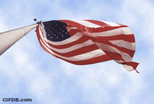 Large American Flag Flying Against Blue Sky GIF