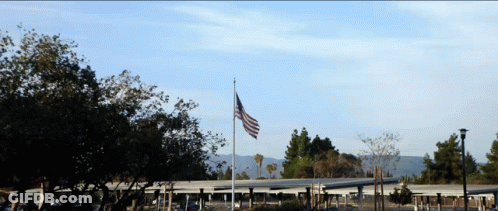 Large American Flag Flying In Front Of Building GIF