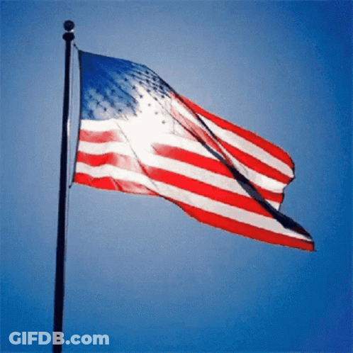 Large American Flag Flying In Wind Blue Sky GIF