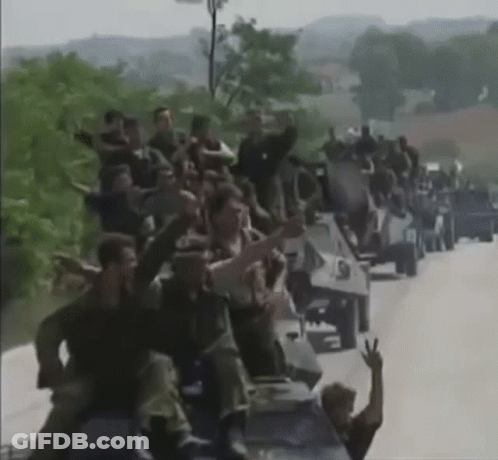 Large Group Sitting On Military Vehicles On Road GIF