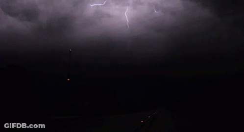 Lightning Strikes Over A Dark Road With A Street Light In The Foreground GIF