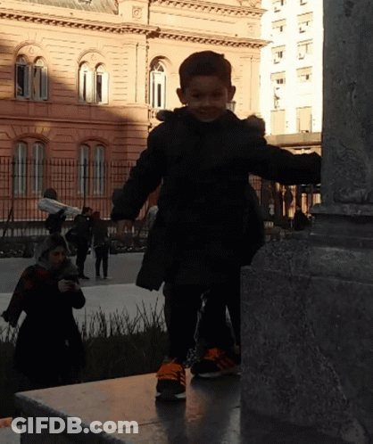 Little Boy In Black Jacket And Orange Shoes On Ledge GIF