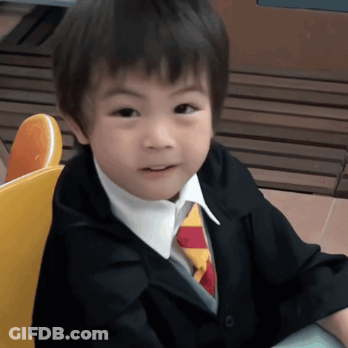 Little Boy In Suit And Tie Sitting In Yellow Chair GIF