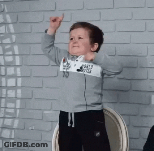 Little Boy In World Coaster Sweatshirt In Front Of Brick Wall GIF