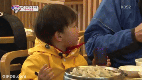 Little Boy In Yellow Jacket Sitting At Table With Bowl Of Food And KB52 Logo GIF